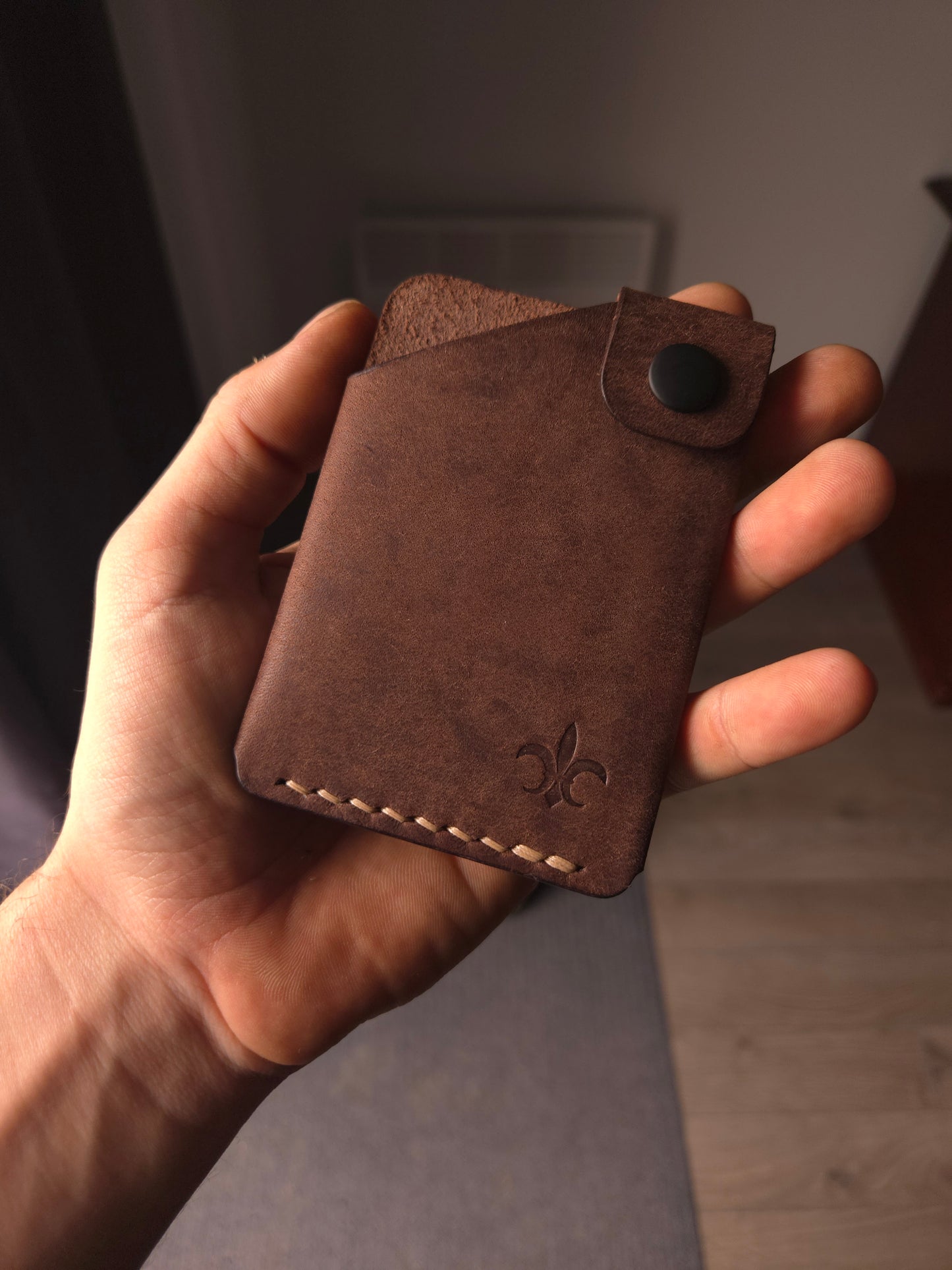 Le Compact leather wallet held in hand showing size and profile.
color is dark brown.