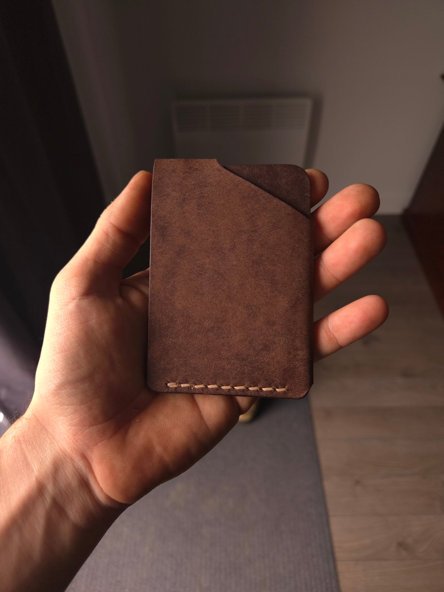 Le Compact leather wallet held in hand showing size and back profile. color is dark brown.