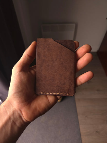 Le Compact leather wallet held in hand showing size and back profile. color is dark brown.