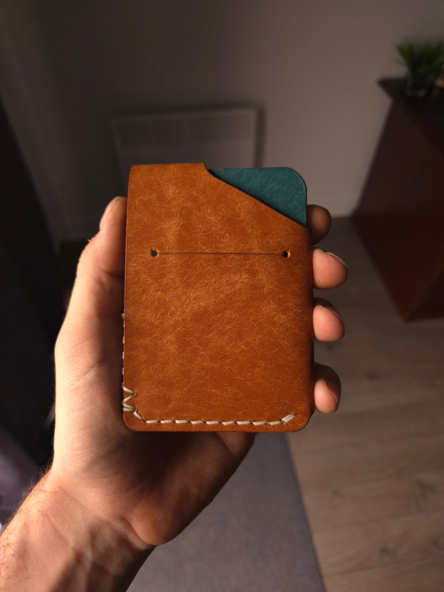 Le Patron leather wallet held in hand showing size and back card access. 
colors are cognac & aqua.