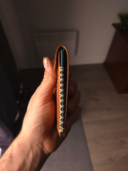 Le Patron leather wallet held in hand showing size and hand saddle stitching detail.
colors are cognac & aqua.