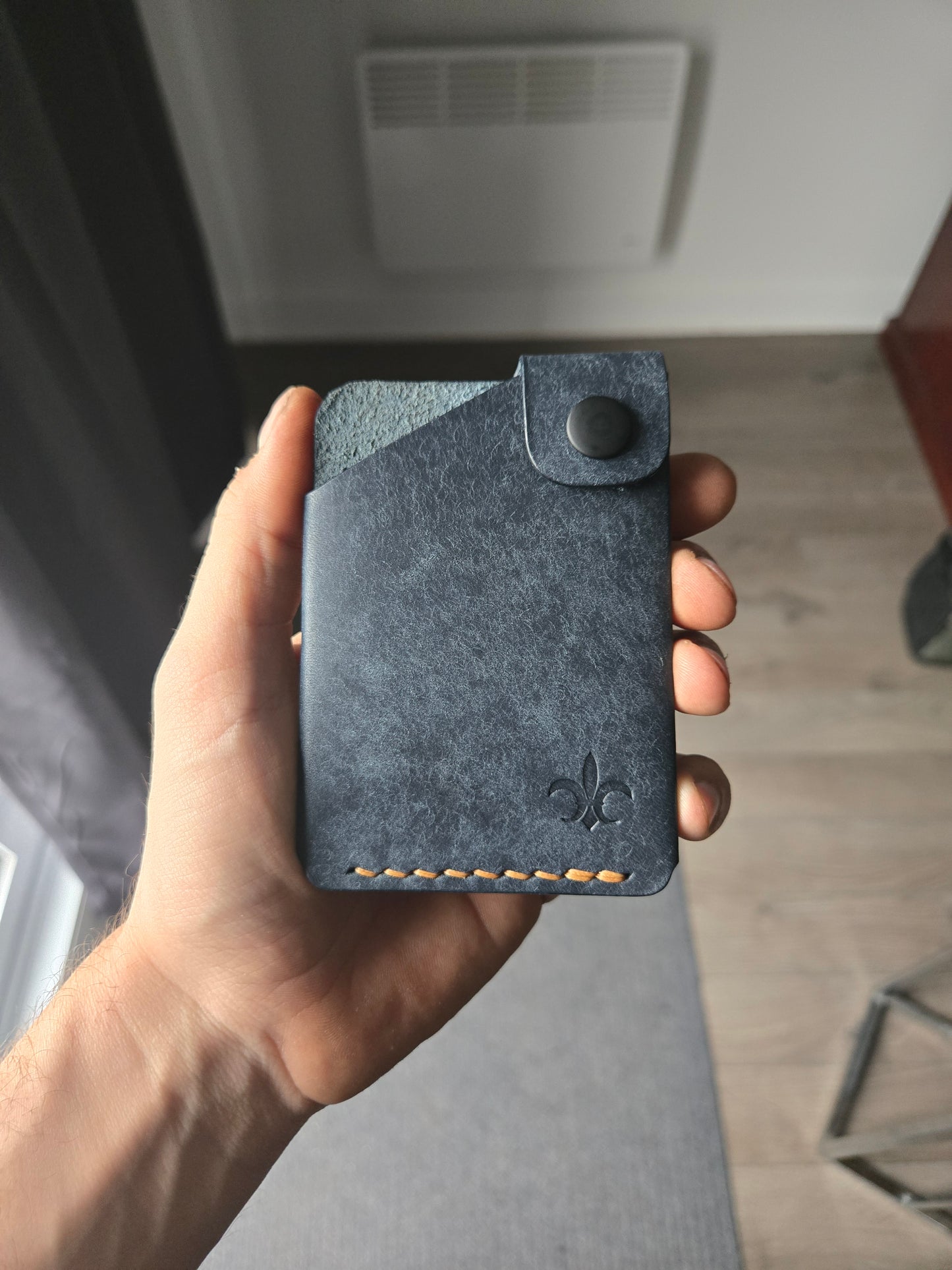 Le Compact leather wallet held in hand showing size and profile.
color is Navy.