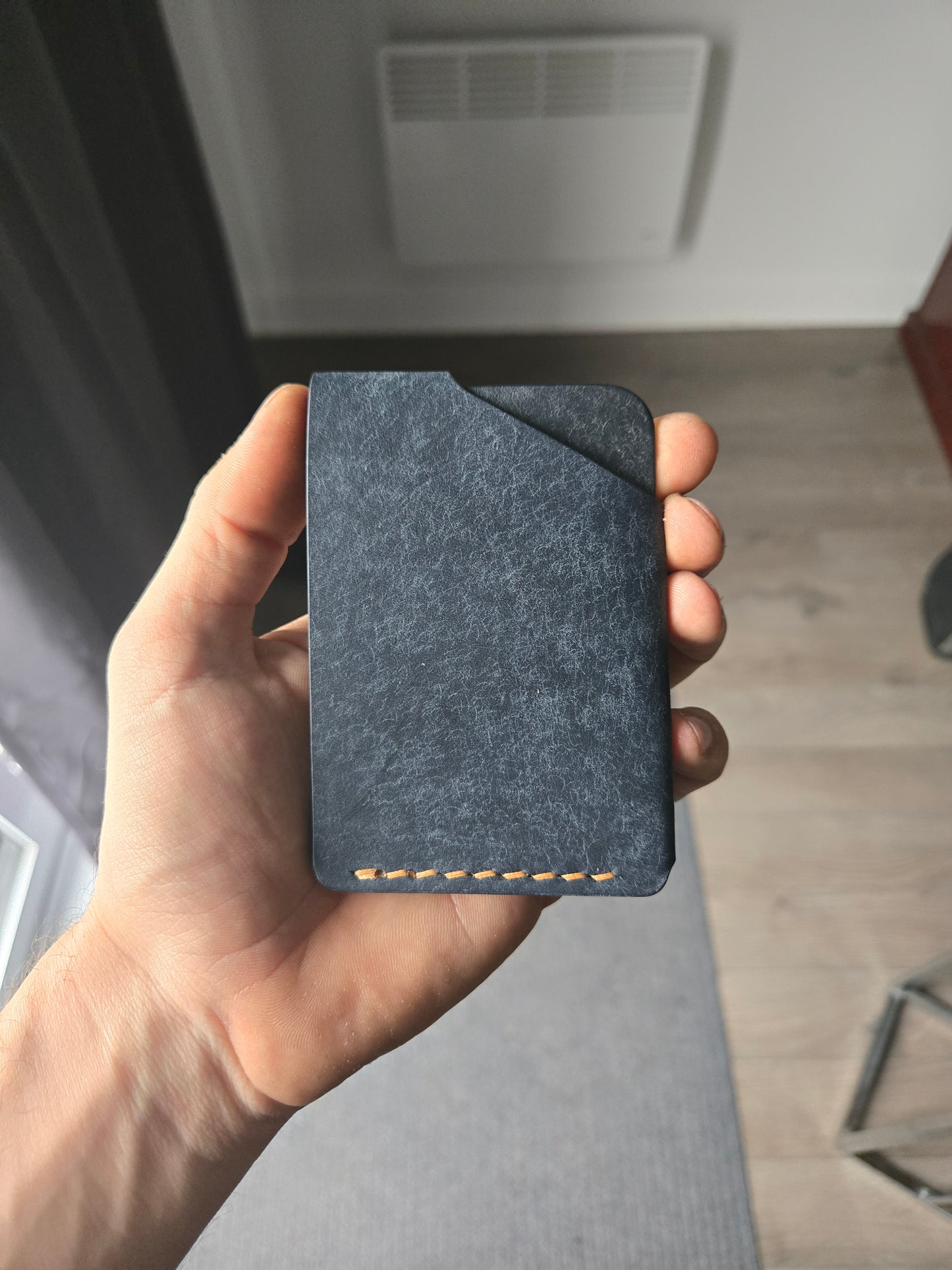 Le Compact leather wallet held in hand showing size and back profile. color is Navy.