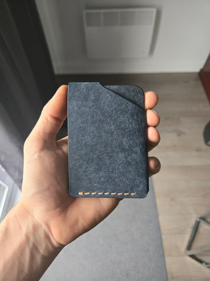 Le Compact leather wallet held in hand showing size and back profile. color is Navy.