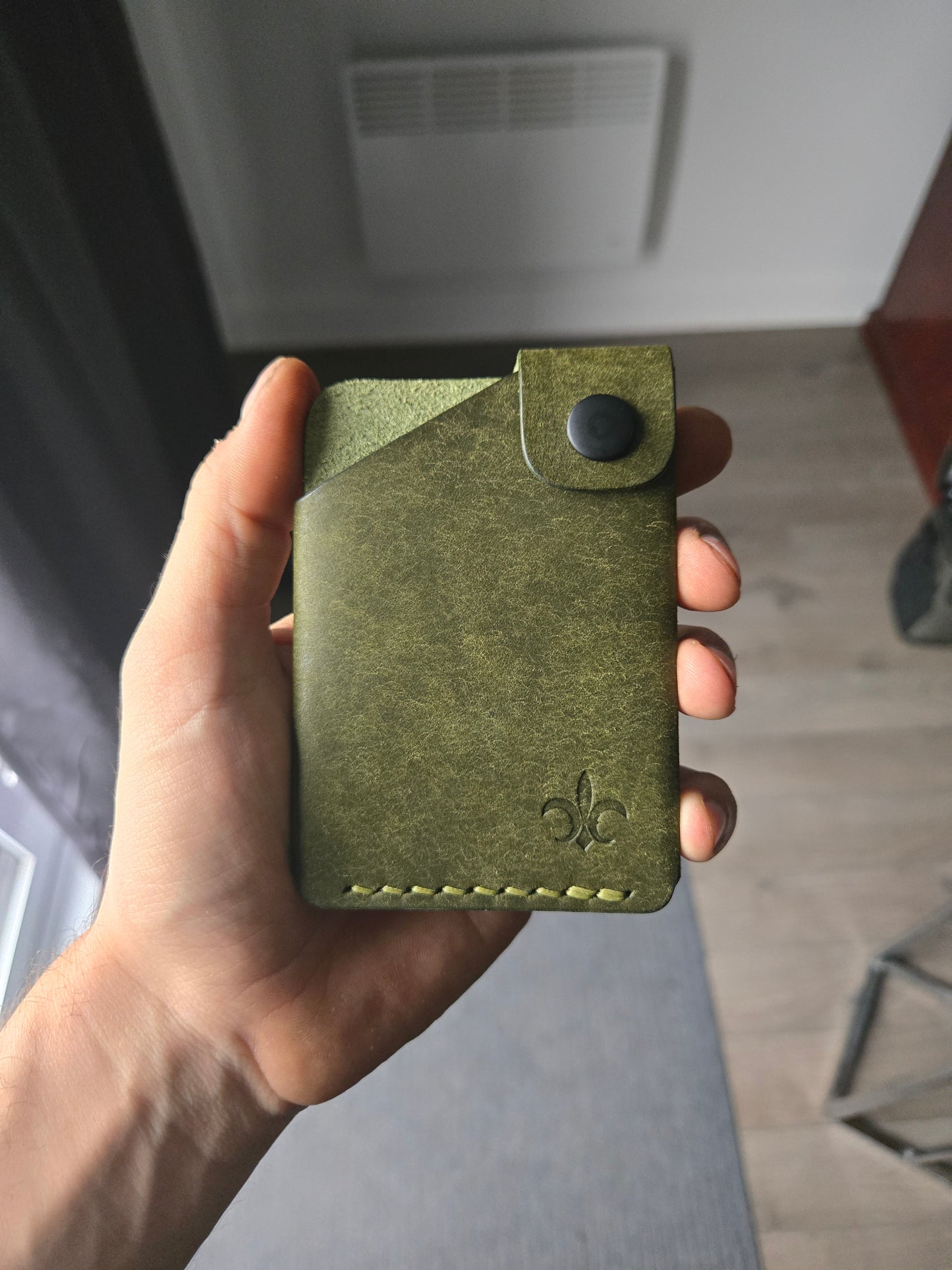 Le Compact leather wallet held in hand showing size and profile.
color is Olive.