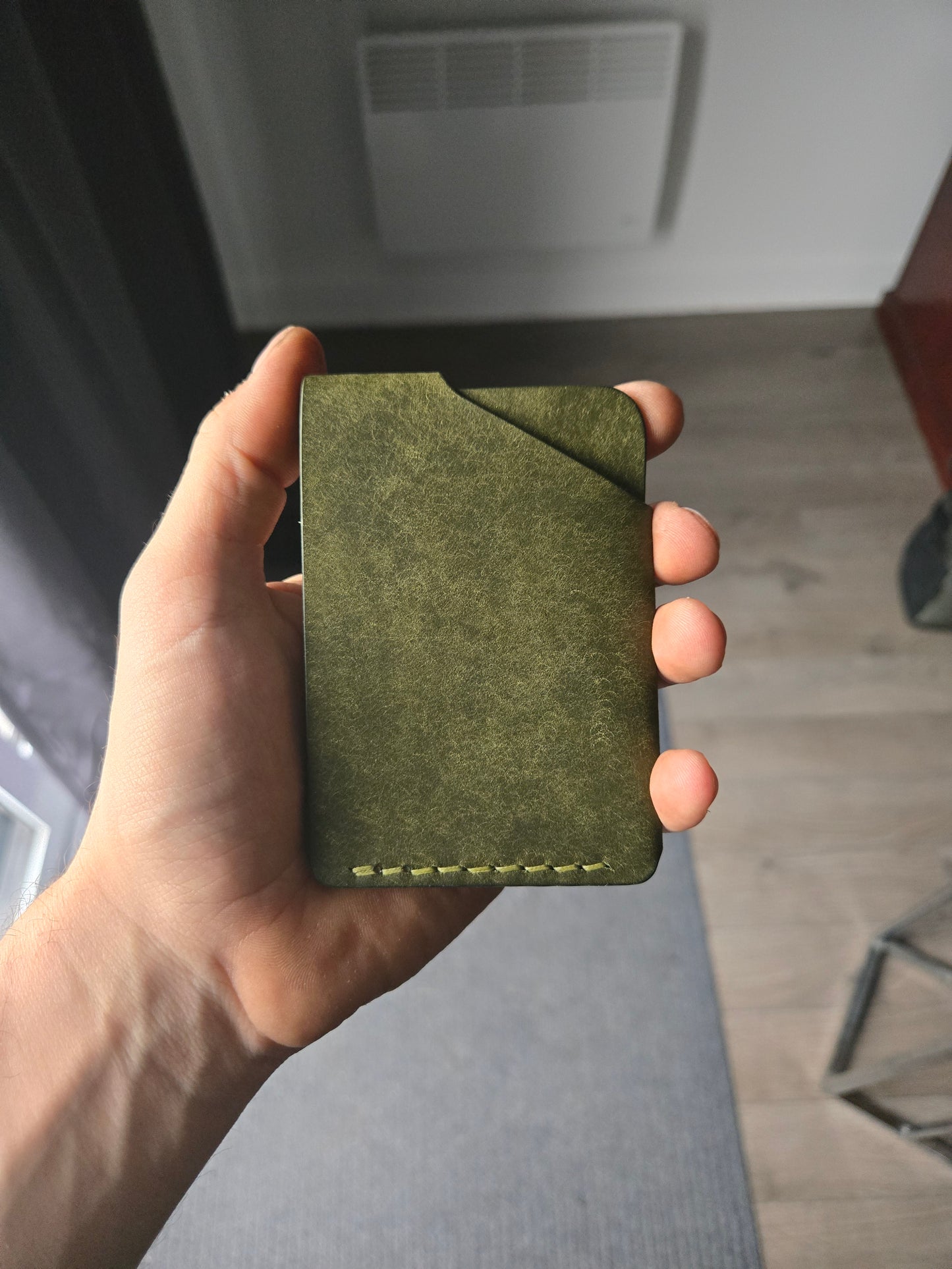 Le Compact leather wallet held in hand showing size and back profile. color is Olive.